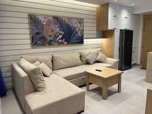 Una sala moderna con un sofá seccional color beige, una mesa de centro de madera y una gran obra de arte floral en la pared.