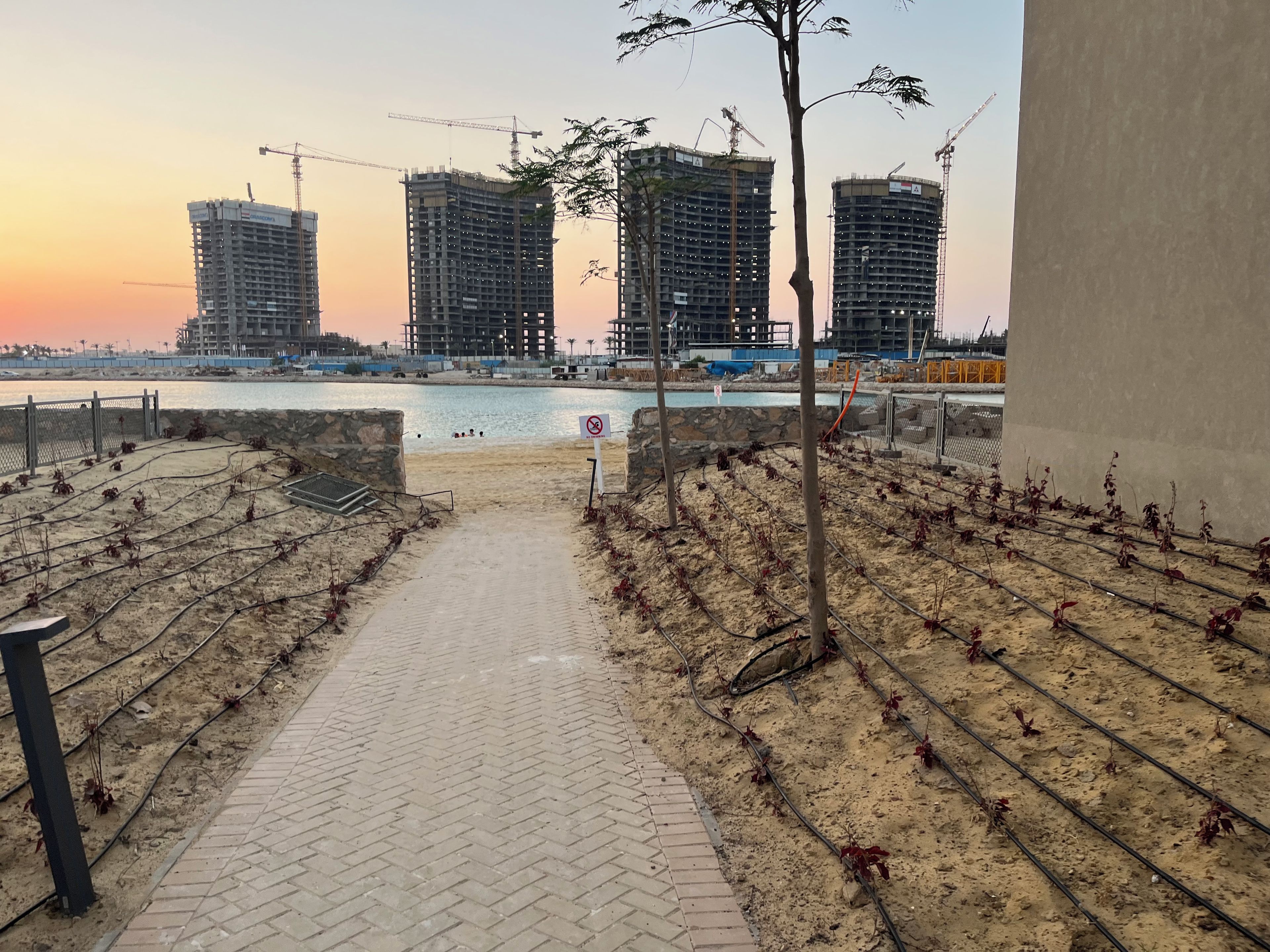 Un sentier qui mène à la promenade en bord de mer, avec des grues de construction et des bâtiments en arrière-plan.