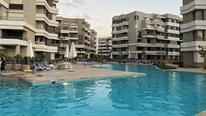 Ein Schwimmbecken mit Liegestühlen und Sonnenschirmen, umgeben von mehrstöckigen Wohnhäusern.