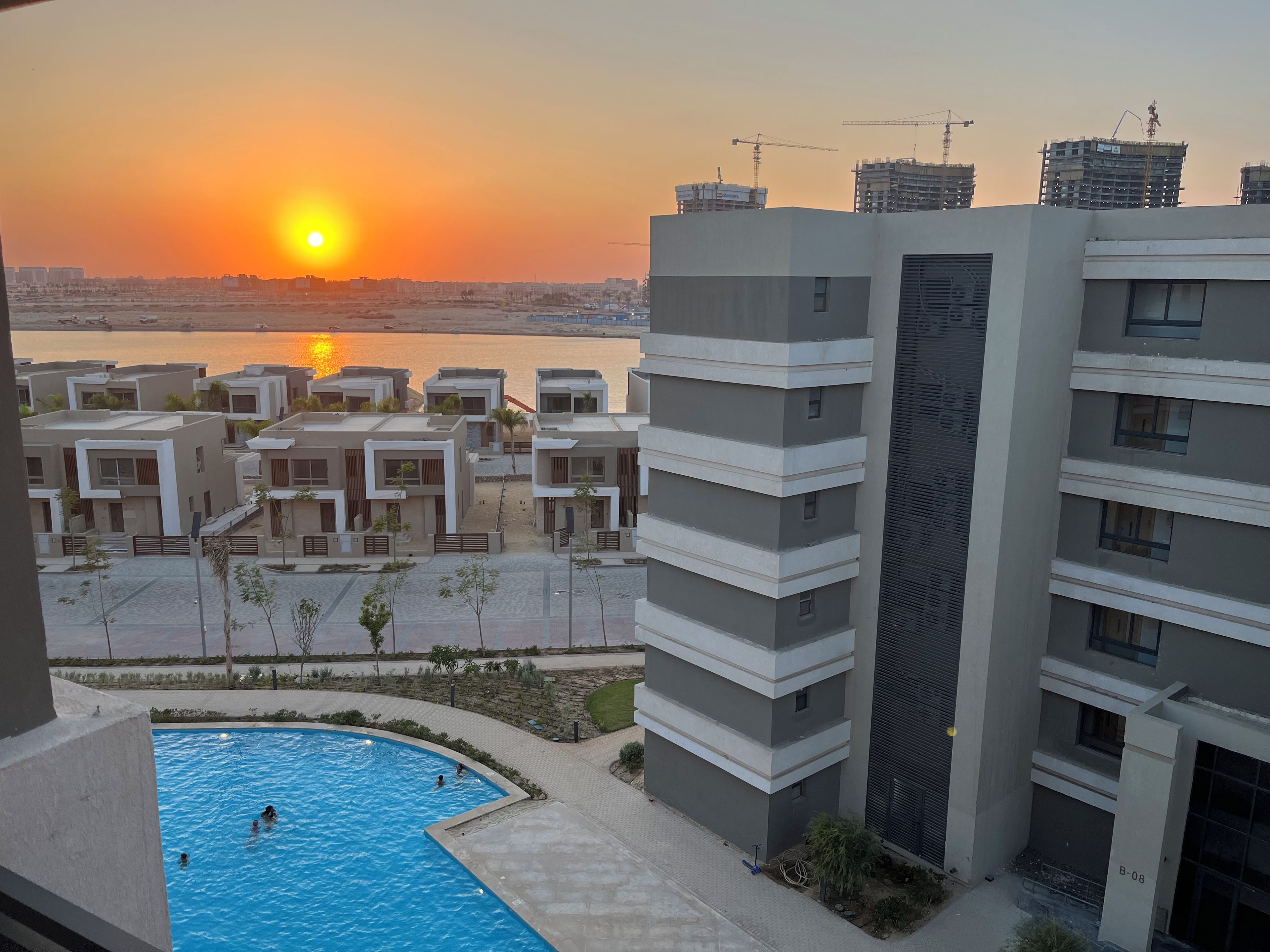 Wohnkomplex mit Schwimmbad, Blick auf den Sonnenuntergang und Baukränen im Hintergrund.