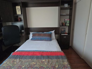 A neatly made bed with a white duvet, a colorful blanket, and a decorative pillow.