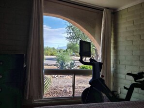 A room with a large arched window, a stationary exercise bike, and a television mounted on the window sill.