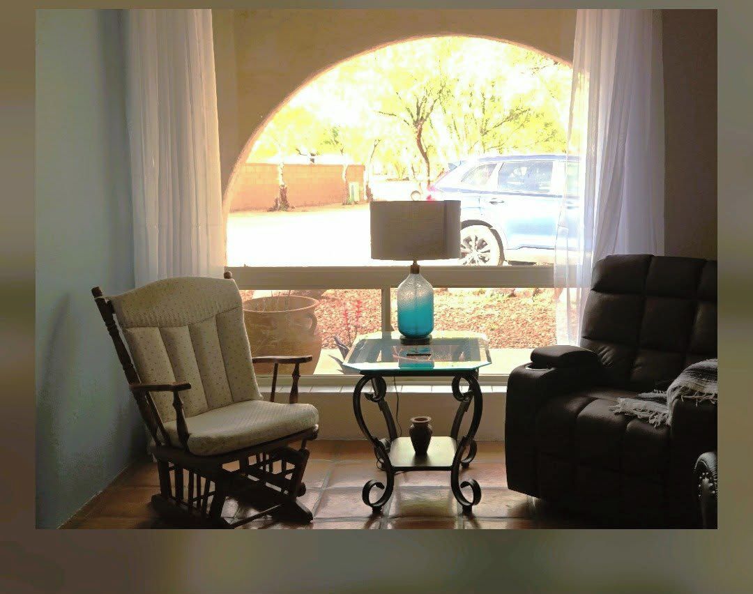 A room with a wooden rocking chair, a black armchair, and a small table with a lamp.