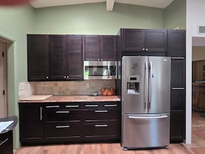 A kitchen with dark cabinets, a stainless steel refrigerator, and a microwave.