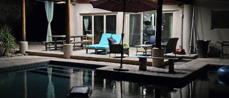 Un espace aménagé au bord de la piscine, avec des chaises longues, une table et un coin salon abrité pour le soir.