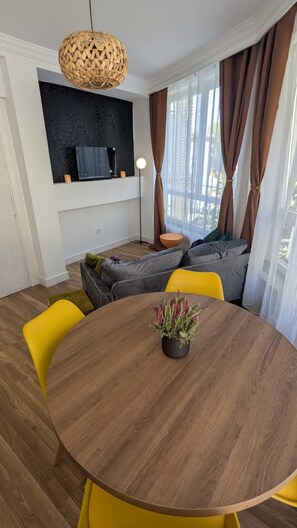 Ein Essbereich mit einem runden Holztisch, gelben Stühlen, einer gewobenen Pendelleuchte und einem schwarzen Wandregal mit einer Kaffeemaschine.