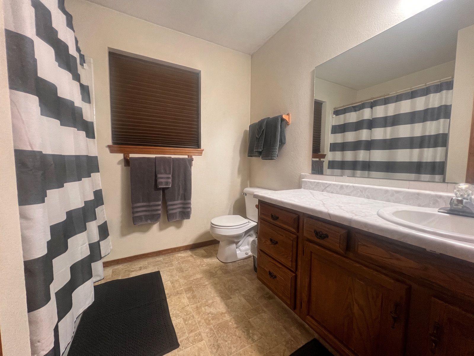 A bathroom with a toilet, a sink, wooden cabinets, a mirror, and a striped shower curtain.