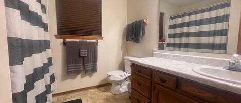 A bathroom with a toilet, a sink, wooden cabinets, a mirror, and a striped shower curtain.