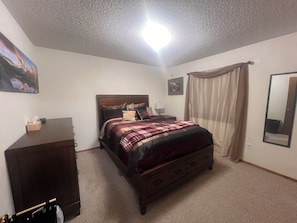 A bedroom with a bed, a dresser, a nightstand, a lamp, a mirror, and a painting on the wall. - 2-bedroom condo in quiet, charming Delta, CO (Delta)