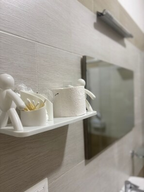 Casa de banho com um armário branco contendo uma caixa de lenços e cotonetes, uma pequena figura branca e um espelho.
