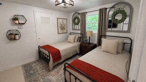 Une chambre avec deux lits, une table de chevet avec une lampe, un radiateur fixé au mur, une fenêtre avec des rideaux et une porte avec une pancarte.