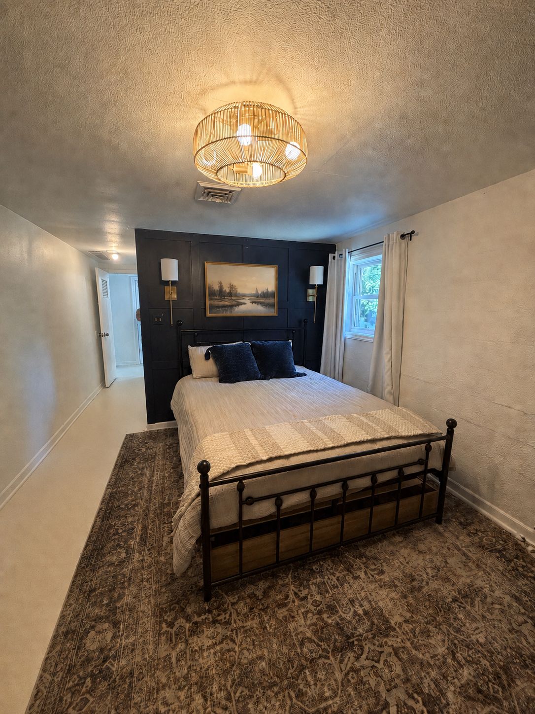 Een slaapkamer met een bed, een schilderij, een lamp en een raam met gordijnen.