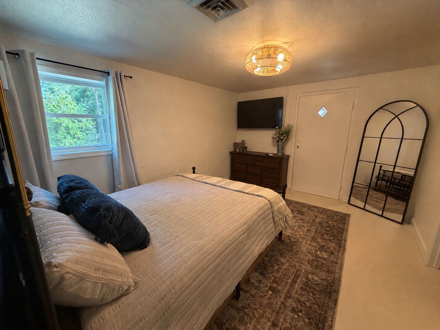 A bedroom with a bed, a dresser, a mirror, and a window.