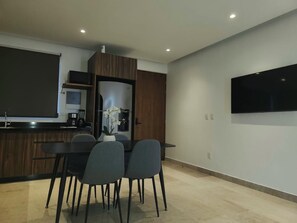 Eine moderne Küche mit Essbereich, einem flachbildfernseher an der Wand und einer kleinen Topforchidee auf der Arbeitsplatte.