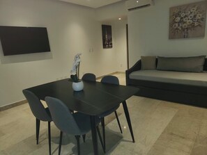 Ein modernes Wohnzimmer mit einem schwarzen Esstisch und Stühlen, einer Couch und einem an der Wand befestigten Flachbildfernseher.