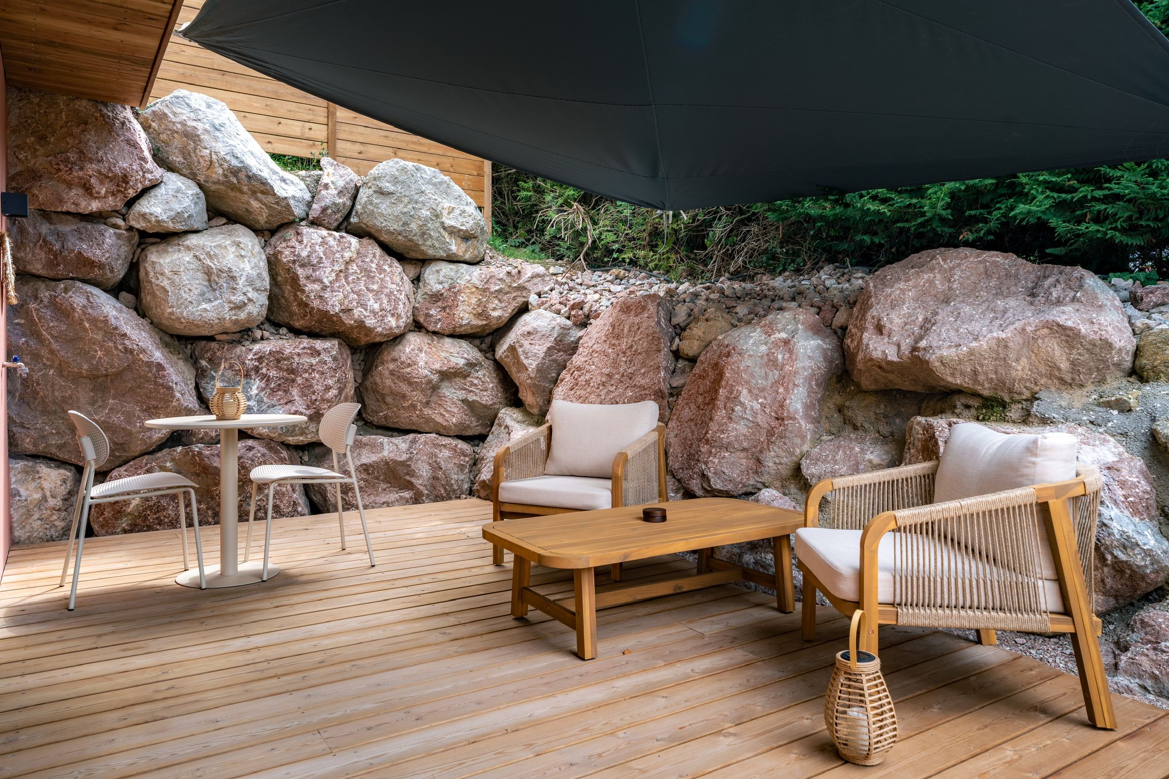 Un espace extérieur aménagé avec une terrasse en bois, un mur en pierre et un grand parasol pour créer de l’ombre.