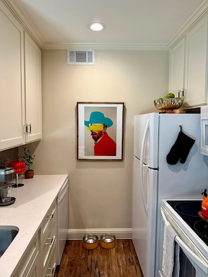 A compact kitchen with white cabinets, a stainless steel refrigerator, a microwave, a coffee maker, and a framed artwork on the wall. - Modern 1BR with Private Yard Near Highland Park (Dallas)