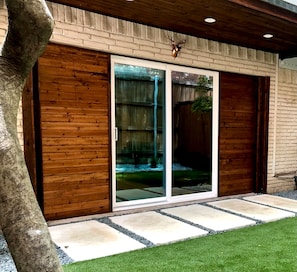A modern building with a wooden facade, large sliding glass doors, and a stone pathway leading to a grassy area. - Modern 1BR with Private Yard Near Highland Park (Dallas)
