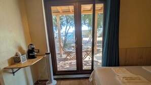 Una habitación con una cama, un escritorio con una radio y un ventanal corredizo que da a un espacio exterior con una mesa y sillas.