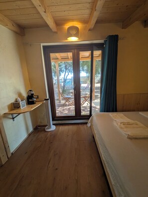 Ein Zimmer mit einem Bett, einem Schreibtisch mit Radio und einer Glastür zu einem Außenbereich mit Tisch und Stühlen.