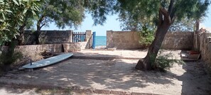 A sandy courtyard with a stone wall, a gate, and a surfboard. - Beach cottage with a bedroom and bathroom (Quartu Sant'Elena)