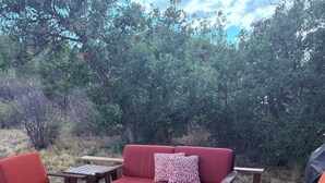 A deck with a red sofa, two wooden chairs, and a small table. - Peaceful 2 bedroom log cabin in Durango perfect for a relaxing getaway. Pets ok. (Durango)