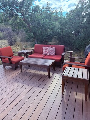 Eine Terrasse mit einer roten Couch, zwei Holzstühlen und einem kleinen Tisch.