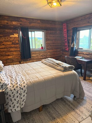 Ein rustikal eingerichtetes Zimmer im Chalet-Stil mit einem Bett, einem Schreibtisch und einem Fenster mit Vorhängen.