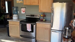 A kitchen with wooden cabinets, a stainless steel refrigerator, a stove, and a water dispenser. - Peaceful 2 bedroom log cabin in Durango perfect for a relaxing getaway. Pets ok. (Durango)