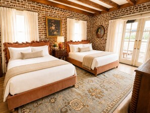 Habitació d'hotel amb dos llits, una paret de maó, sostre de fusta i una alfombra amb dibuixos.