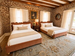 A room with two beds, a brick wall, and a large window with curtains. - Aunt Toren's Room at Keystone Hotel - 303 (Savannah)