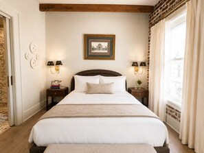 A hotel room with a large bed, two bedside tables with lamps, a framed picture on the wall, and a window with curtains. - Uncle Ngoan's Room at Keystone Hotel - 301 (Savannah)