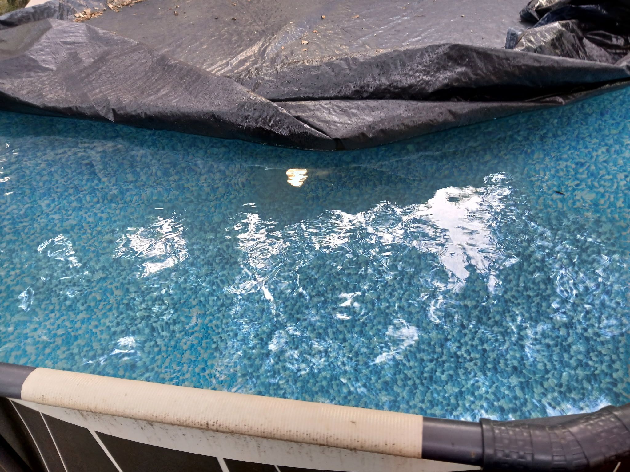 Piscina transparente com boa visibilidade da água e uma lona preta cobrindo parte da área da piscina.