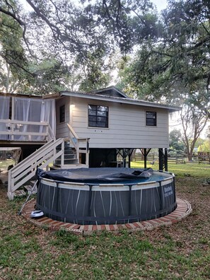 A two-story house with a covered deck and a circular swimming pool.