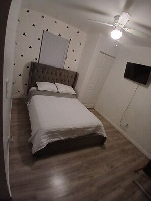 A bedroom with a bed, a ceiling fan, a TV mounted on the wall, and a door.