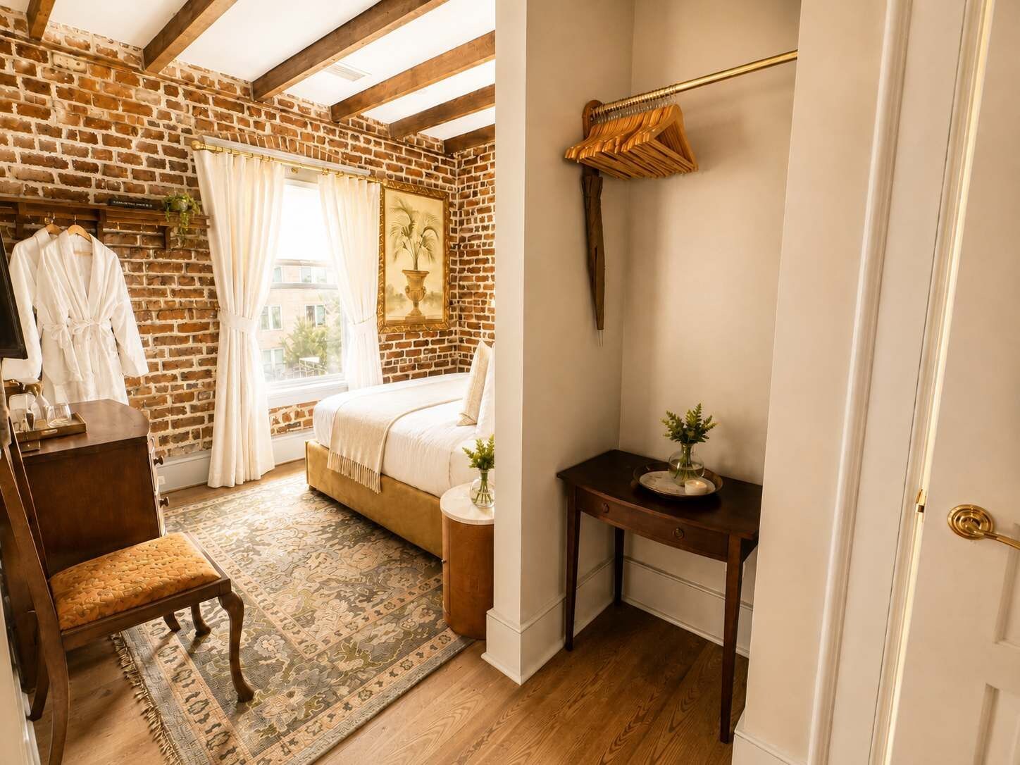 Ein Schlafzimmer mit Backsteinwand, einem Bett, einem Holzstuhl, einem kleinen Tisch mit einer Vase und einem Fenster mit Vorhängen.