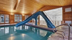 Une piscine intérieure avec un toboggan bleu et des escaliers menant à un niveau supérieur.