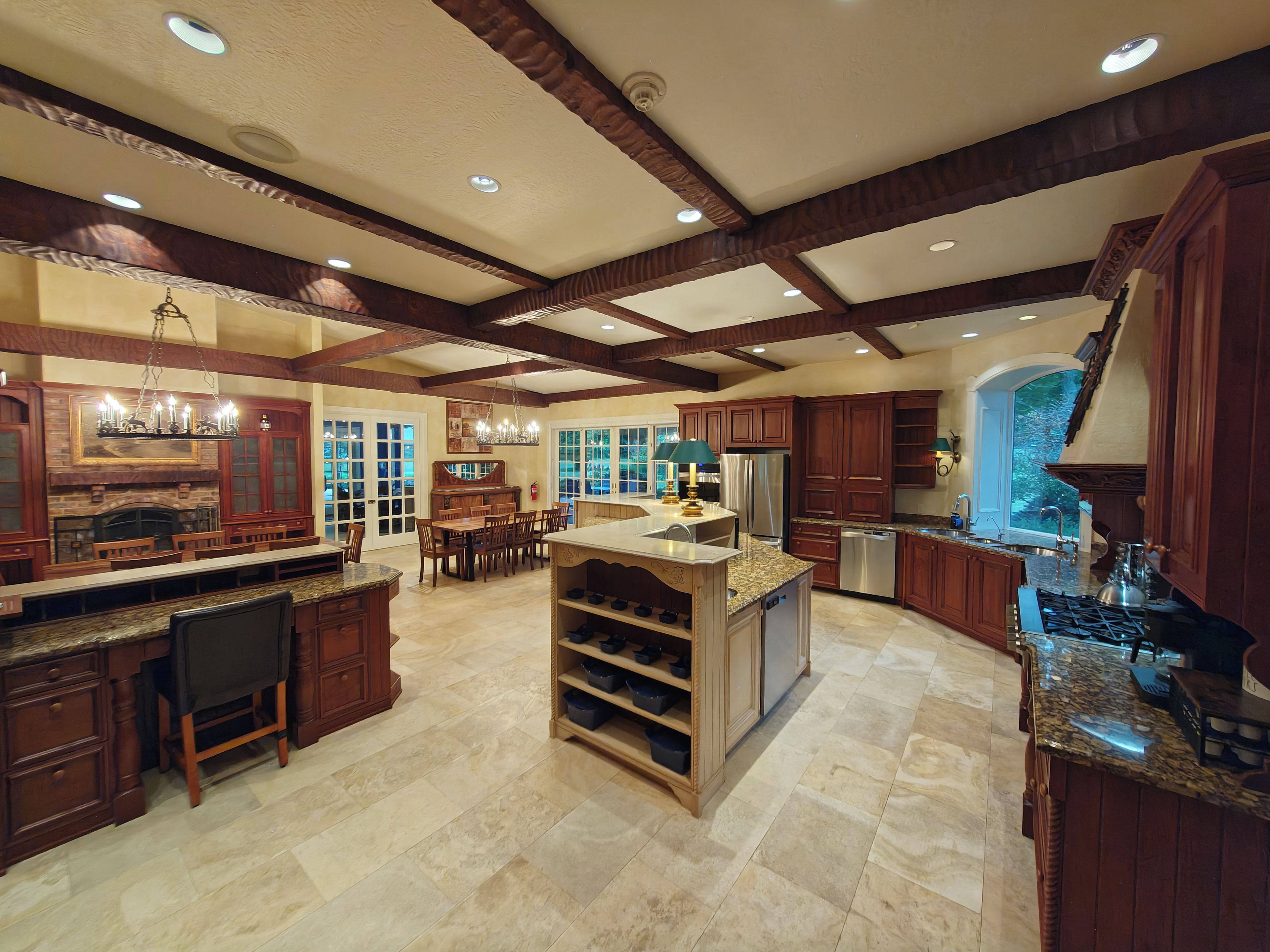 A spacious kitchen with a large island, wooden cabinetry, and a stone tile floor.