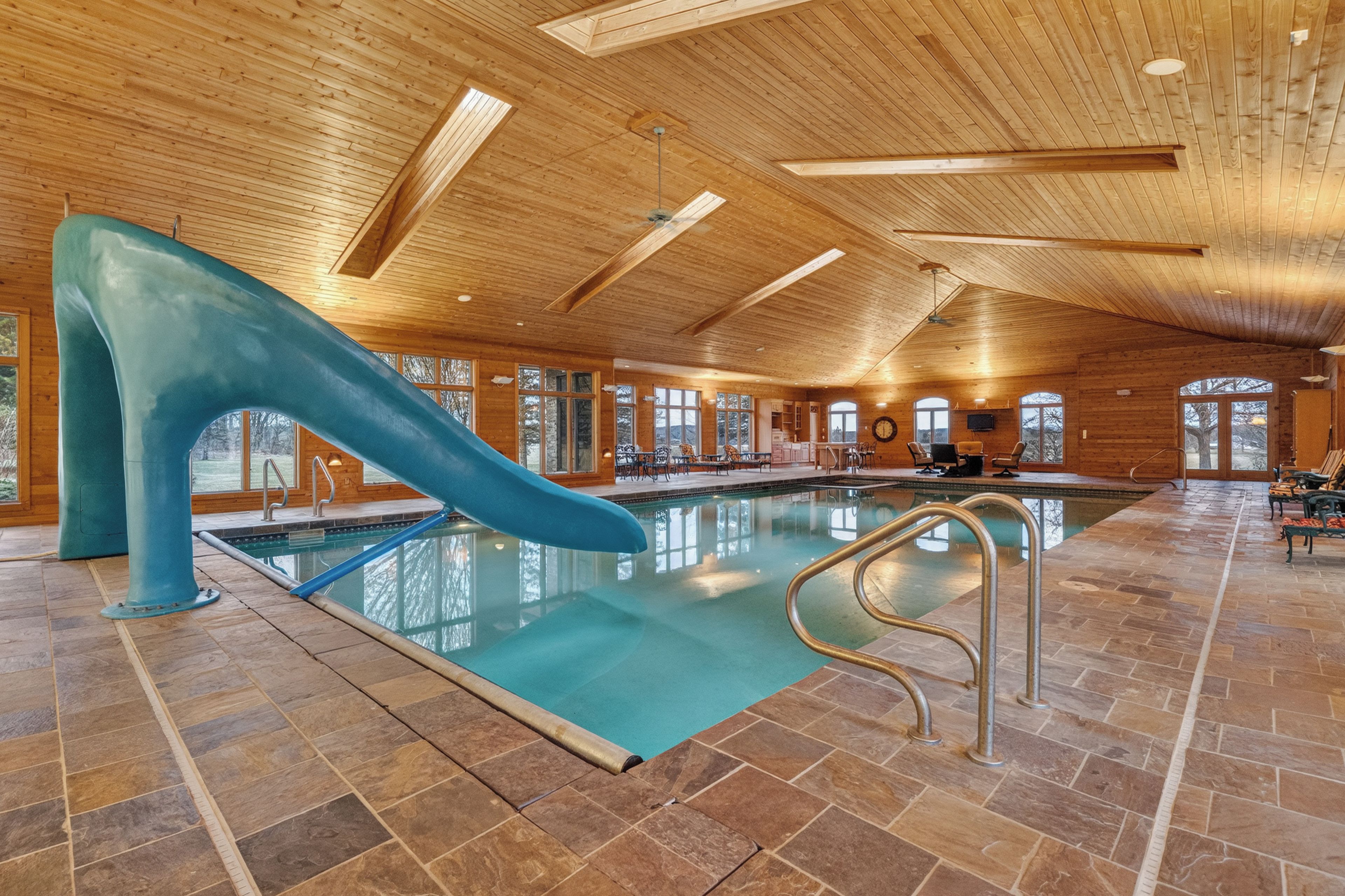 En indendørs swimmingpool med rutsjebane, træloft og stengulv.