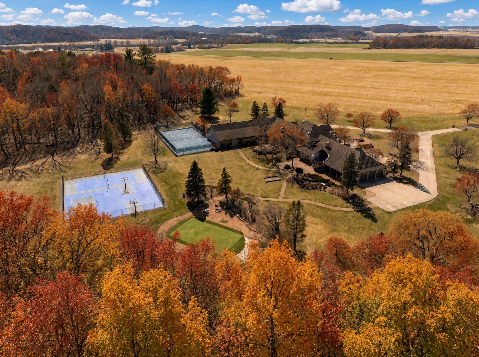 A residential area with a large house, a tennis court, and surrounding autumn foliage.