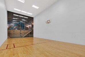 Une salle de sport intérieure spacieuse, dotée d’un plancher en bois, d’un panier de basket et d’une grande fenêtre donnant sur un escalier en bois.