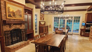 Une salle à manger spacieuse avec une grande table et des chaises en bois, une cheminée avec un manteau en pierre et un lustre.