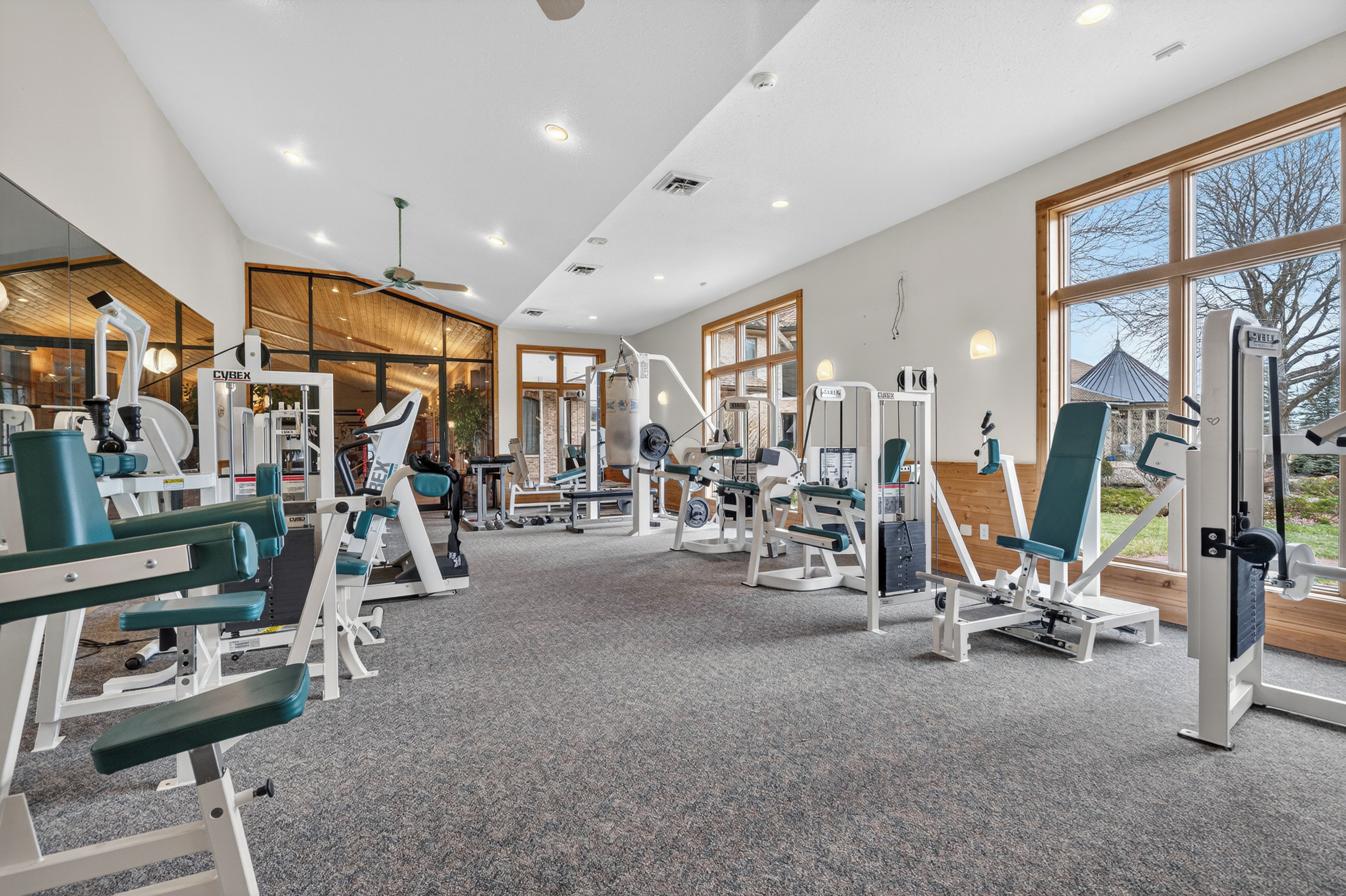 Et fitnesscenter med diverse træningsmaskiner, store vinduer og en loftsvifte.