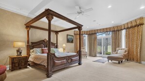Un lit à baldaquin, un coin salon avec un fauteuil et une vue à travers une porte vitrée.