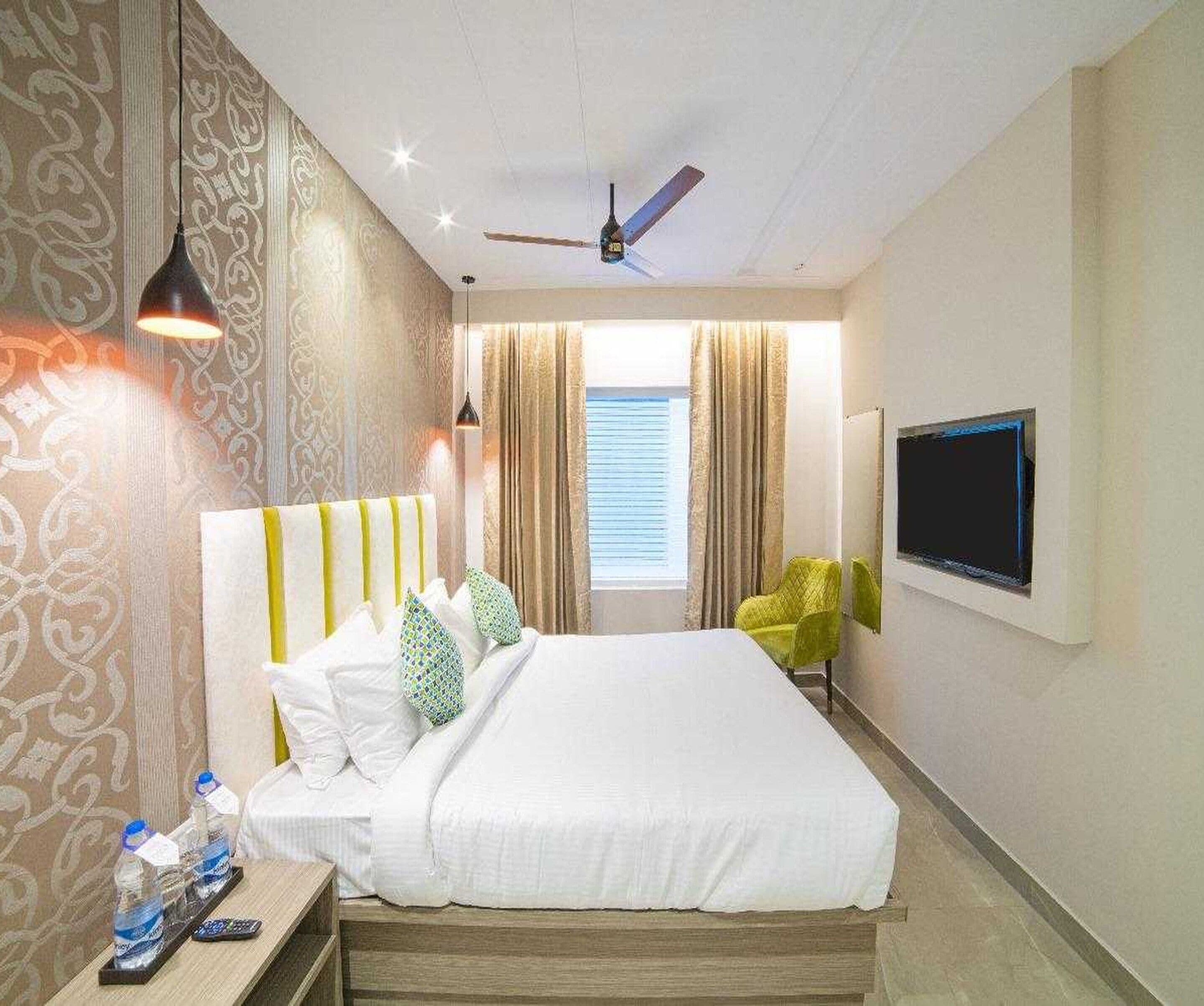 A hotel room with a bed, curtains, a television, and a ceiling fan.