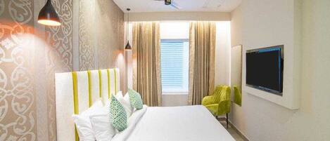 A hotel room with a bed, curtains, a television, and a ceiling fan.