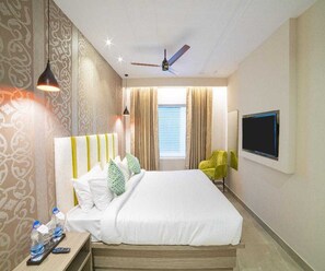 A hotel room with a bed, curtains, a television, and a ceiling fan. - Deluxe King Room Beacon Palette (Visakhapatnam)