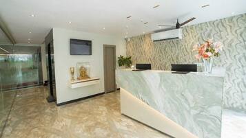 Ein Hotel-Rezeptionsbereich mit einer Marmor-Rezeption, einem Wand-Fernseher und einem Deckenventilator.