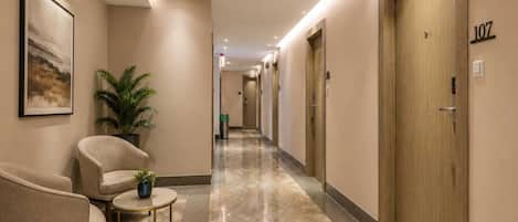 A hotel hallway with a marble floor, a seating area with chairs and a small table, and doors on the right side.