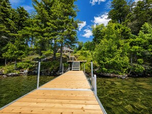 A wooden dock leading to a house surrounded by dense green trees and clear water.